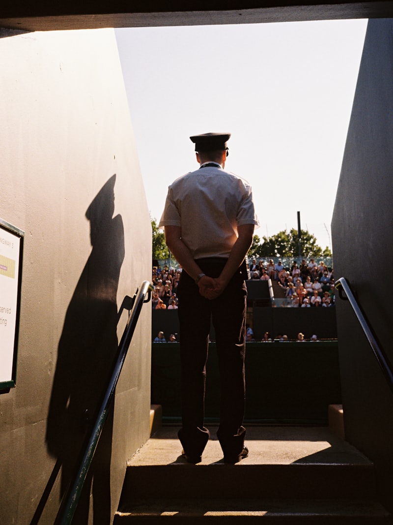 A steward in uniform stands at the top of a gangway, looking out over a crowded stand.